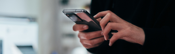 UUna persona che tiene uno smartphone con entrambe le mani, aggiornandosi su notizie relative a questioni doganali.